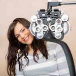 Portrait of happy young woman sitting behind phoropter during eye exam